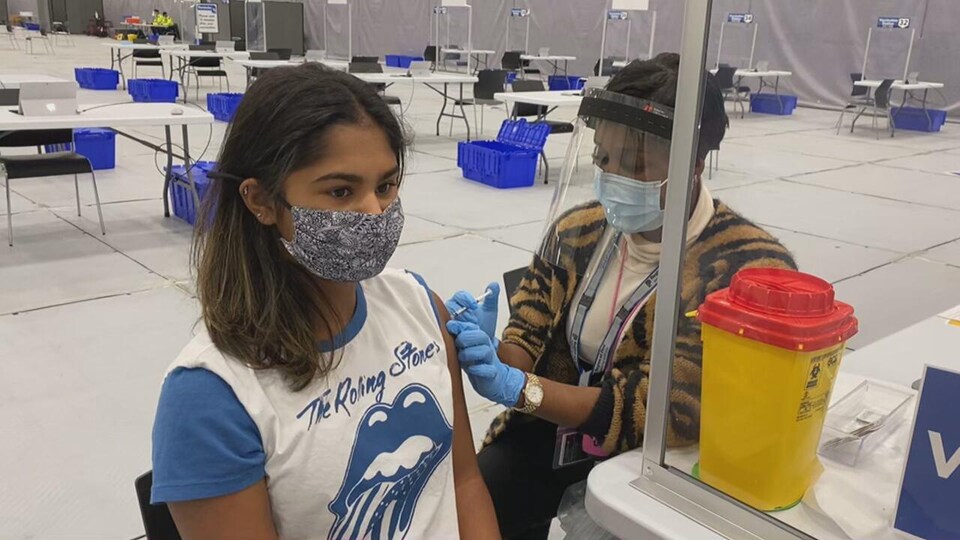 Une jeune fille masquée reçoit un vaccin