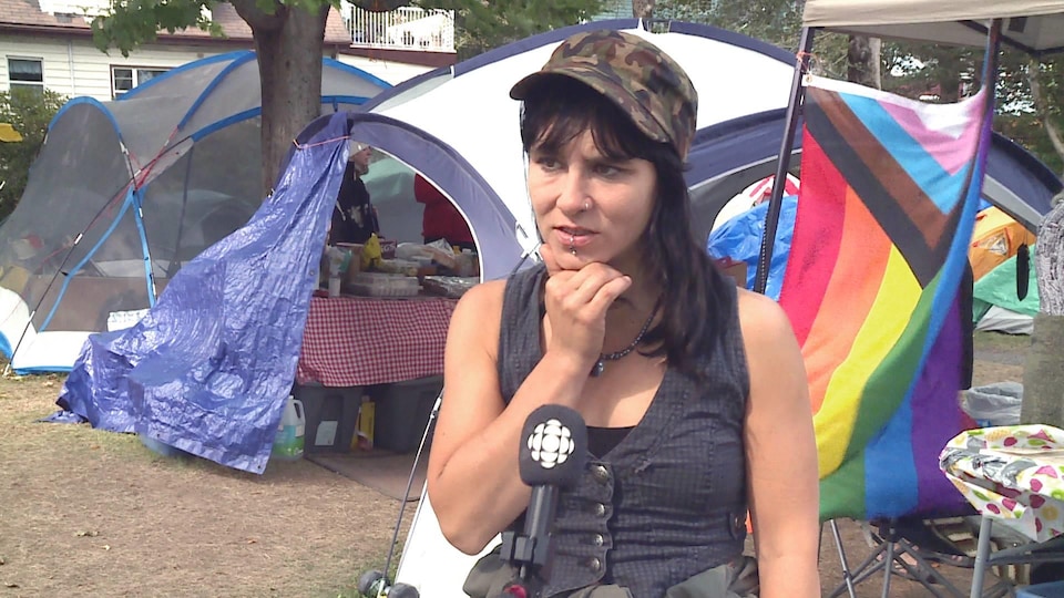 Une femme en entrevue dans un parc devant des tentes.