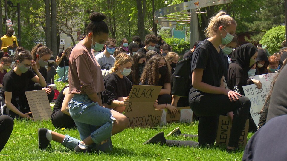 Un groupe de jeunes posent le genoux par terre, signe de solidarité envers les personnes racisées victimes de violence policière.
