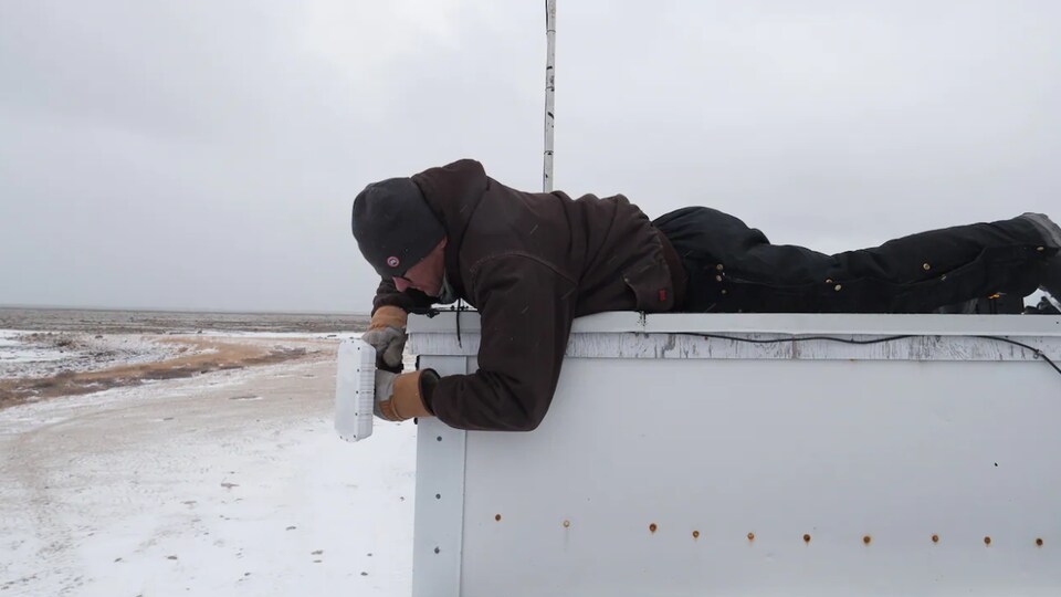 The man lying on the roof of a tower fixes a small radar on the wall.