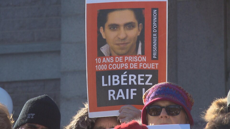 Une personne tient une pancarte de Raif Badawi dans ses mains.