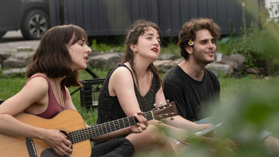 Trois personnes chantent et jouent de la guitare assises dans le gazon.