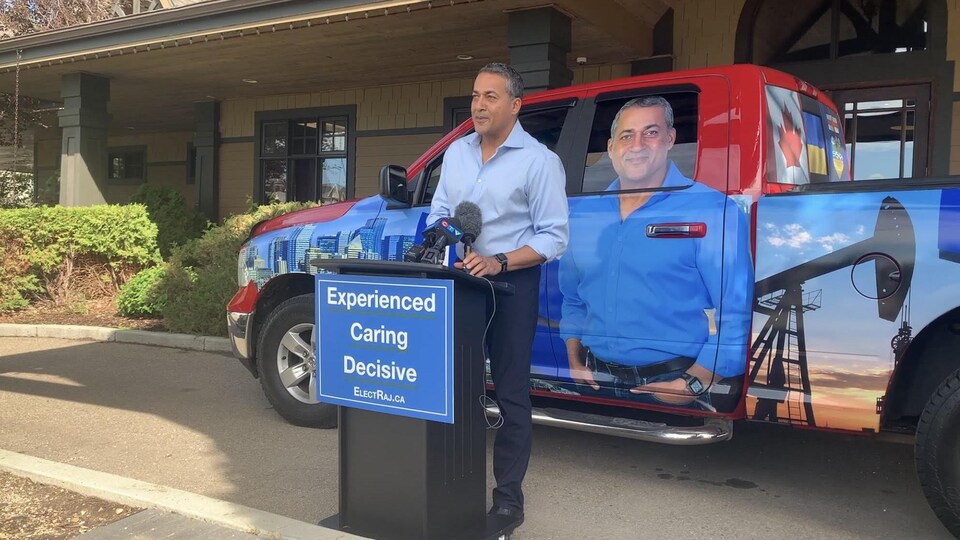 Raj Sherman parle devant un podium, devant un camion à son effigie.