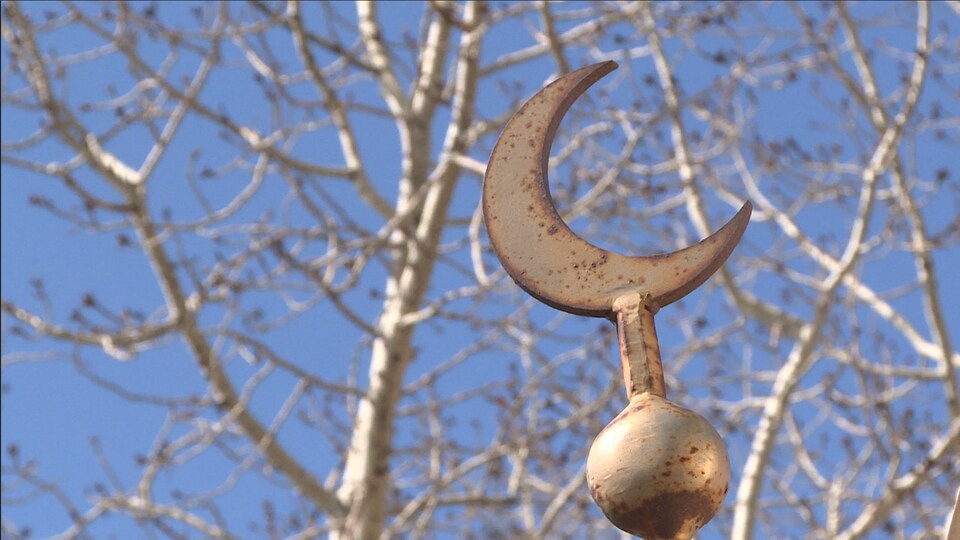 Un croissant de lune symbolique de l'Islam légèrement rouillé devant un arbre.