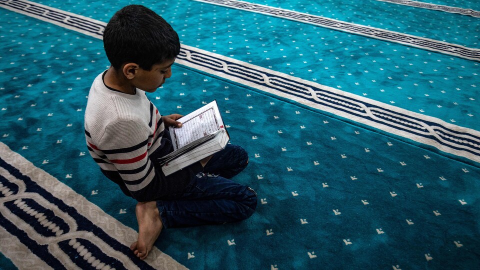 Un enfant lit le coran sur un tapis de prière.