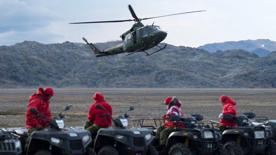 Des Rangers assis sur des VTT regardent un hélicoptère se poser.