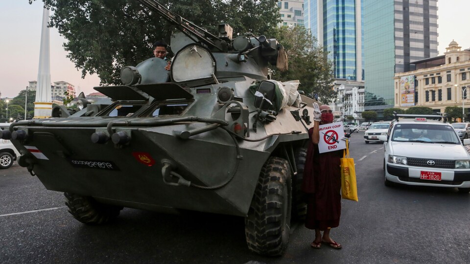 Un char blindé au milieu de la route, en pleine ville, et un manifestant portant une pancarte demandant la fin du coup d'État. 