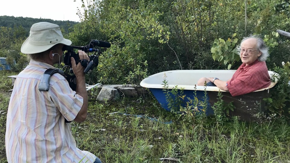 Un caméraman capte des images de Raôul Duguay, assis dans un bain dehors en forêt.