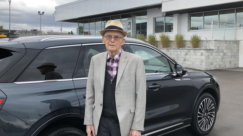 Raoul Perron devant une voiture à l'extérieur.