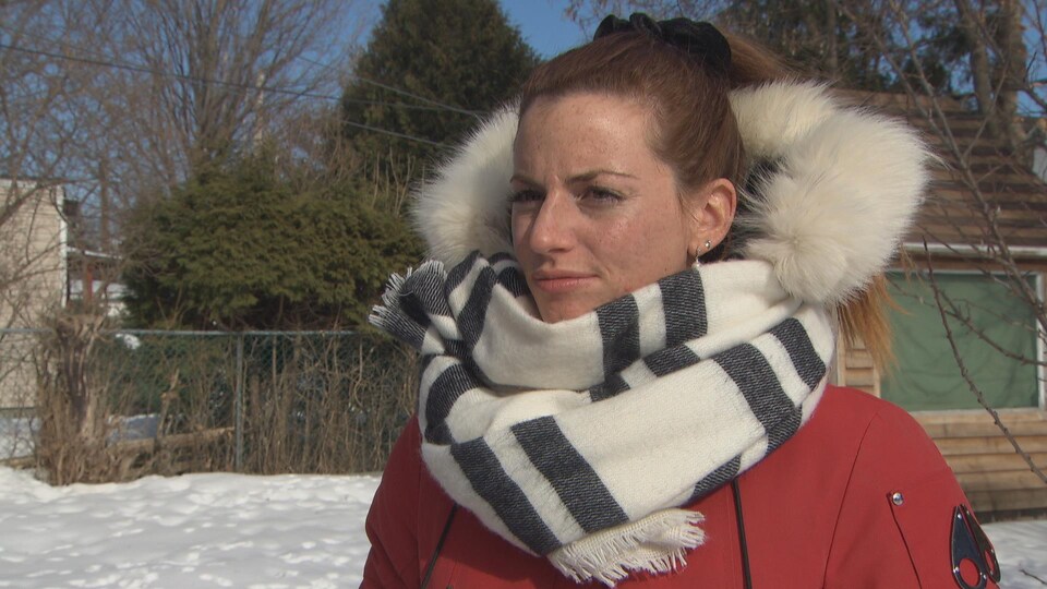 Une jeune femme avec un manteau d'hiver donne une entrevue à l'extérieur.