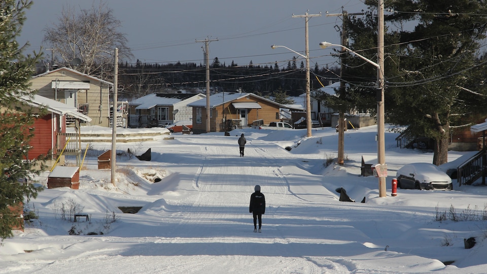 Vue d'ensemble sur la communauté : des maisons, un chemin enneigé et deux personnes qui marchent de dos sur le chemin. 