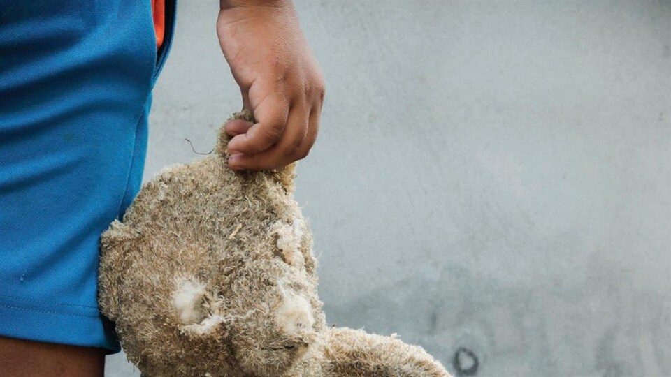 Un enfant tient par l'oreille un nounours en mauvais état.