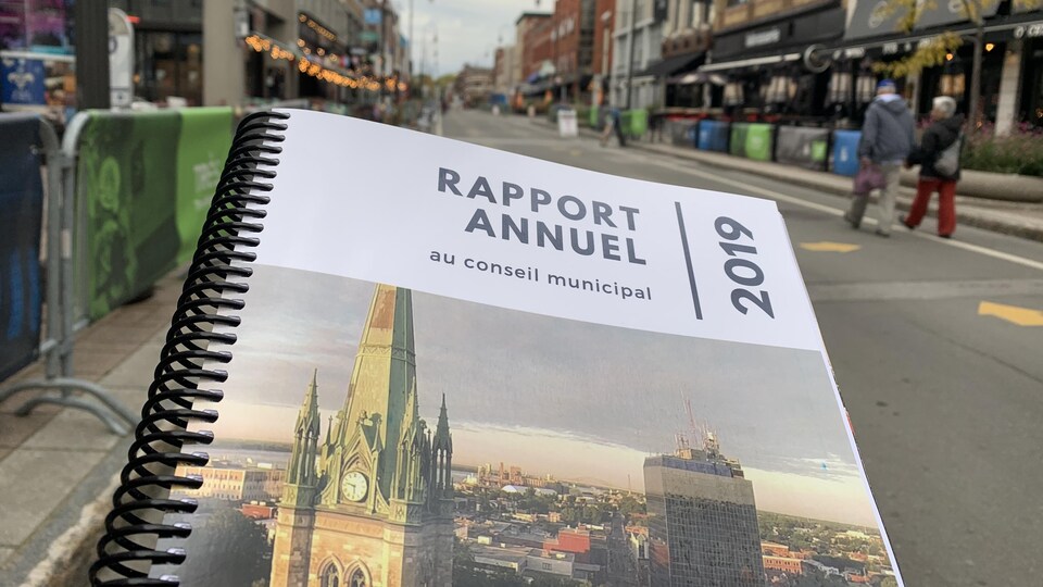 Cahier du rapport annuel devant une rue du centre-ville de Trois-Rivières.