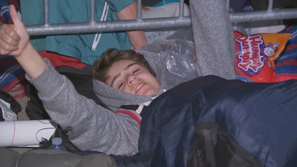 Photo d'un jeune homme couché qui se lève un bras, le pouce dans les airs.