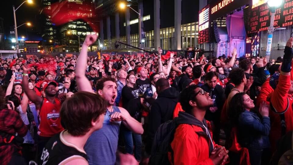Une foule regarde l'écran où est diffusé le match des Raptors lors du premier match de la finale avec des personnes qui crient et ont le poing levé.