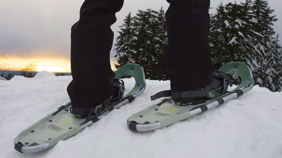 Les jambes d'une personne en raquettes sur la neige.