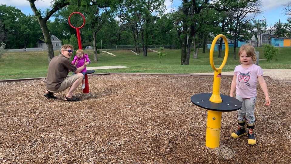 Un père joue avec ses deux filles dans un parc.