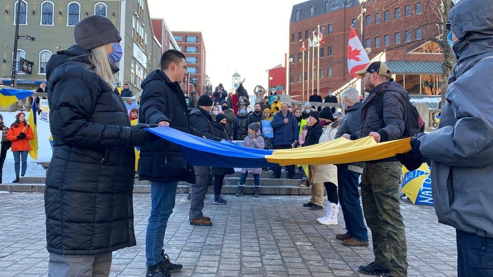 Des gens debout sur une place publique, face à face, tenant ensemble un drapeau de l'Ukraine.