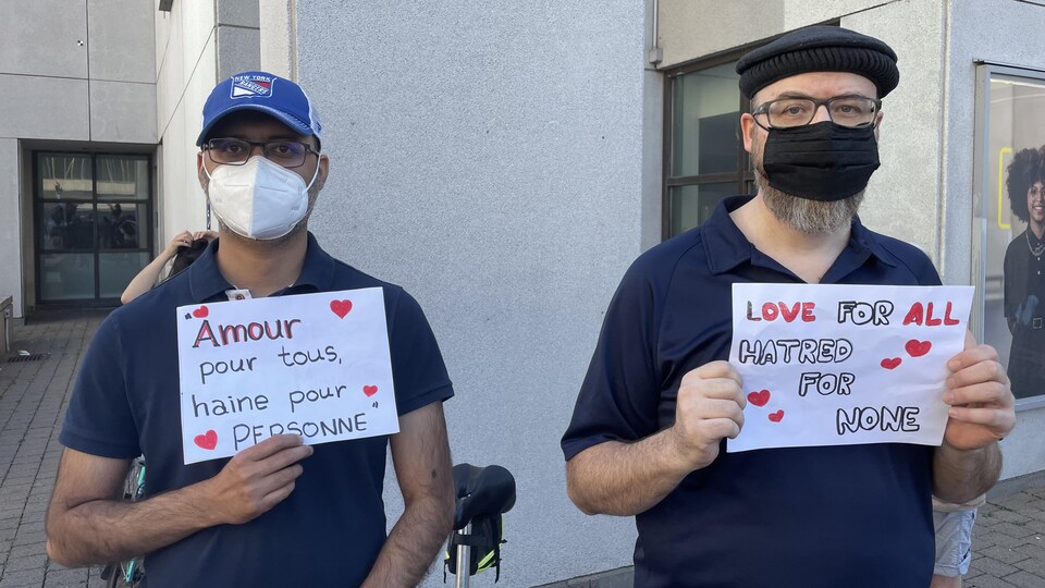 Un homme masqué tient une feuille de papier sur laquelle on peut lire : « Amour pour tous, haine pour personne ». Un autre tient une feuille affichant le même message en anglais.