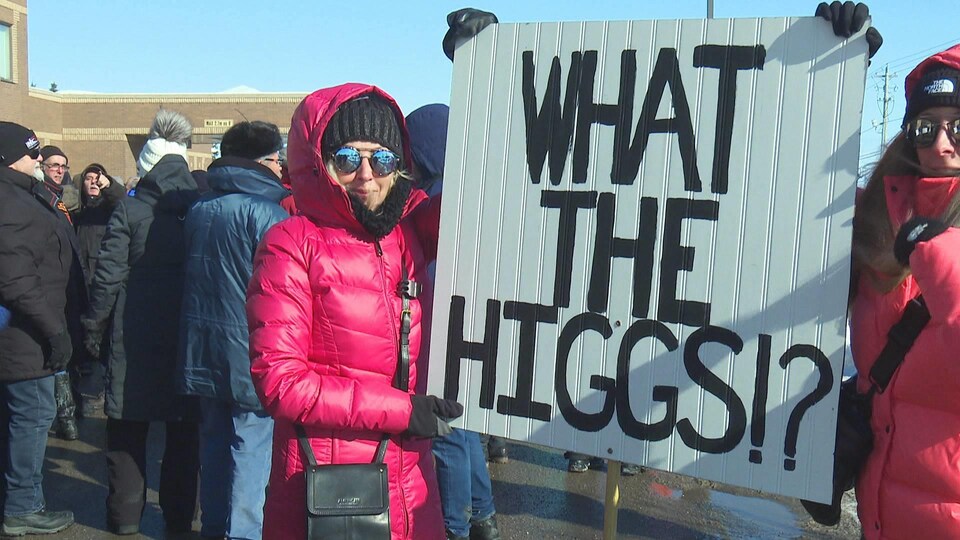Deux femmes vêtues en rose tiennent une grande affiche sur laquelle on peut lire «What The Higgs!?»