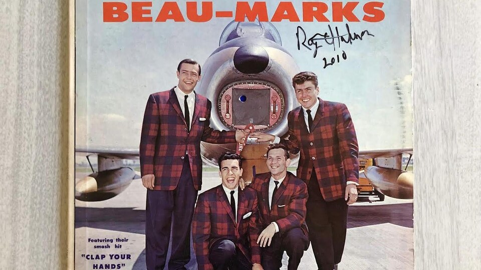 Quatre hommes posent devant un avion sur une couverture d'album de musique.