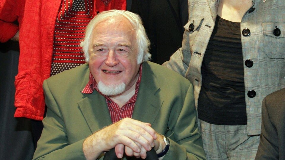 Il est assis et tient sa canne devant lui.
