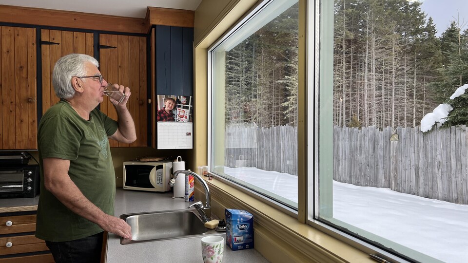 Raynald Murphy boit un verre d'eau devant sa fenêtre.