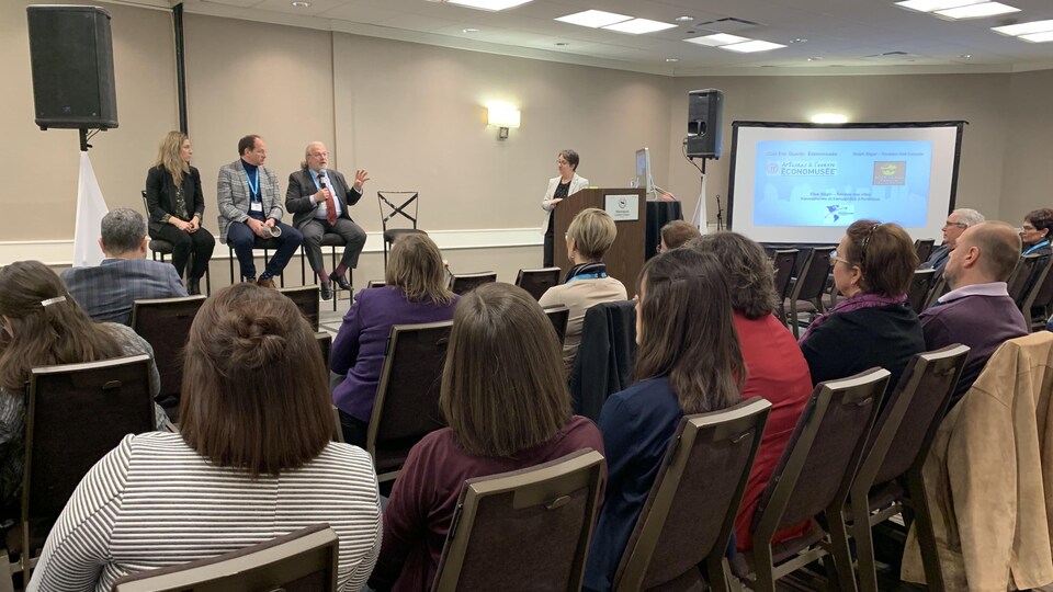 Un panel de trois personnes parle devant une dizaines de personnes dans une salle de conférence.