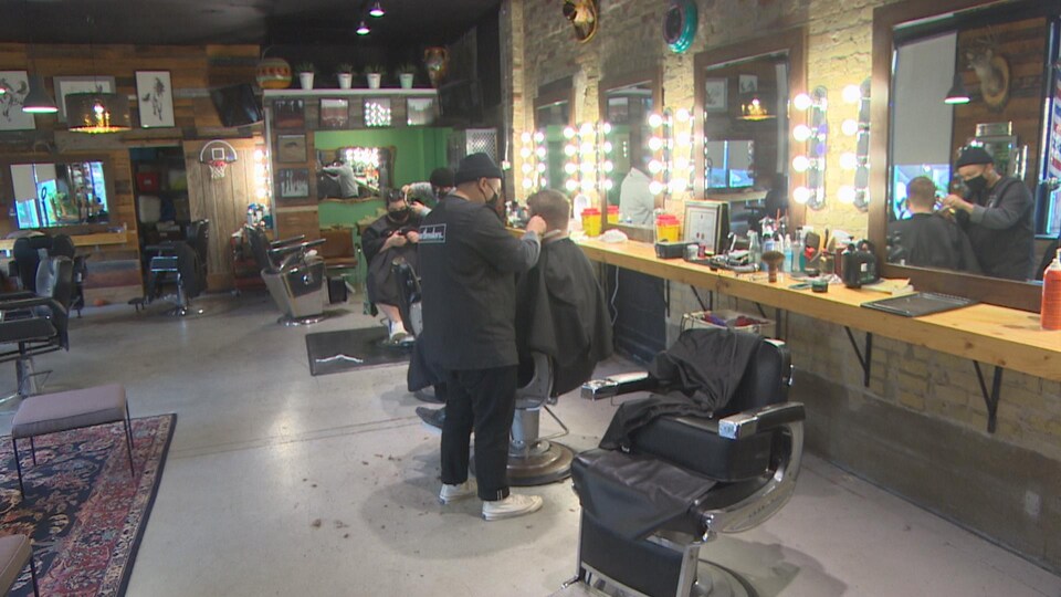 Des coiffeurs coupent les cheveux d'hommes dans un salon de coiffure de Winnipeg.