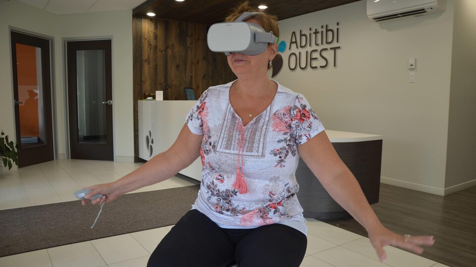 Une femme porte un casque de réalité virtuelle et tient ses mains levées, comme si elle touchait quelque chose.