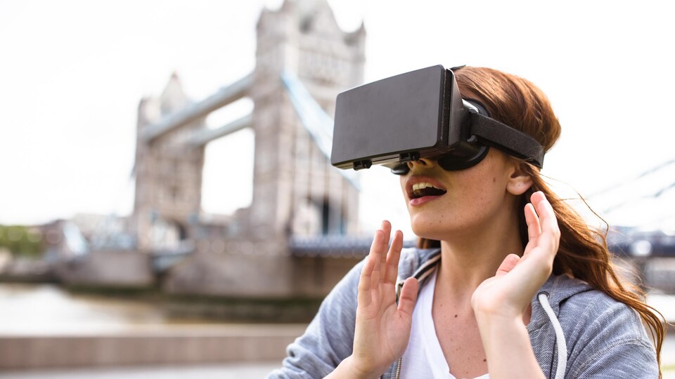 Une femme en train d'utiliser un masque de réalité virtuelle près du Tower Bridge de Londres.
