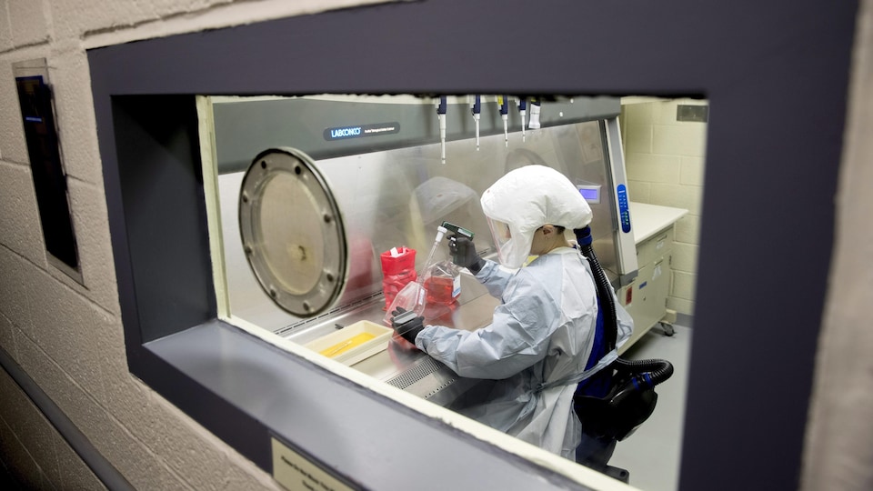 Une femme portant un habit de protection manipule des instruments de laboratoire.