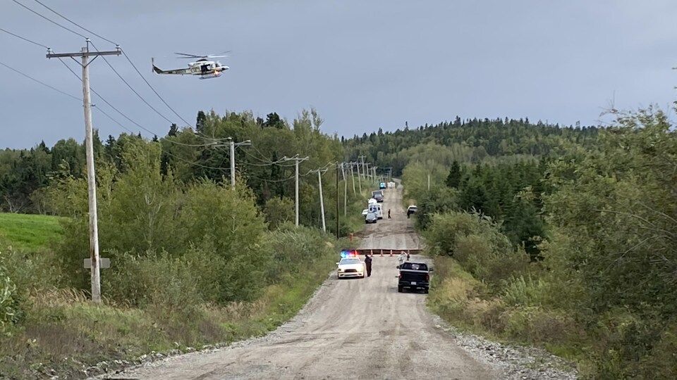 Des véhicules d'urgence et un hélicoptère près d'une route de gravier affaissée.