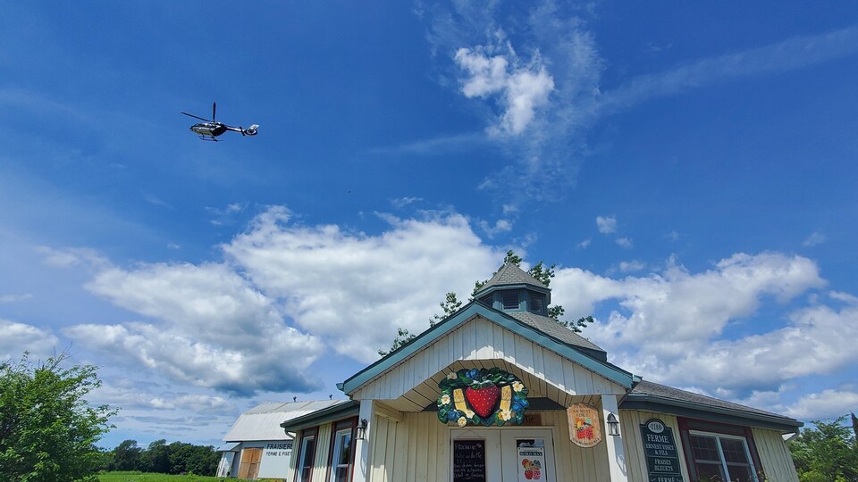 Un hélicoptère dans le ciel survole un bâtiment de ferme.