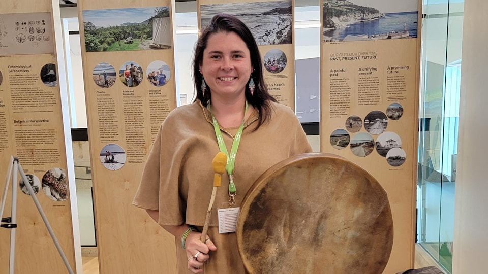 Kalika Sinnett portant des habits traditionnels autochtones avec à la main un tambour. 