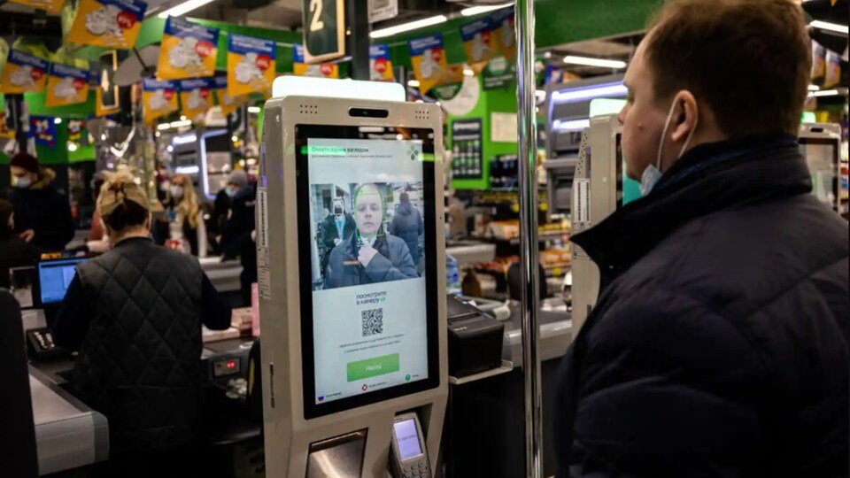Un homme retire son masque pour faire détecter son visage par une caisse empruntant la technologie de la reconnaissance faciale dans une épicerie.