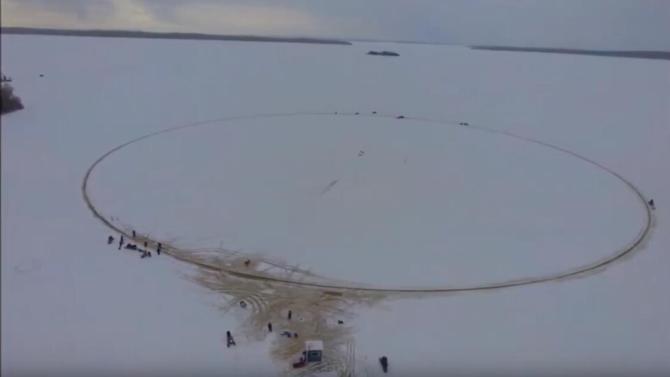 Vue de haut d'un grand cercle sur un lac glacé avec des gens autour.