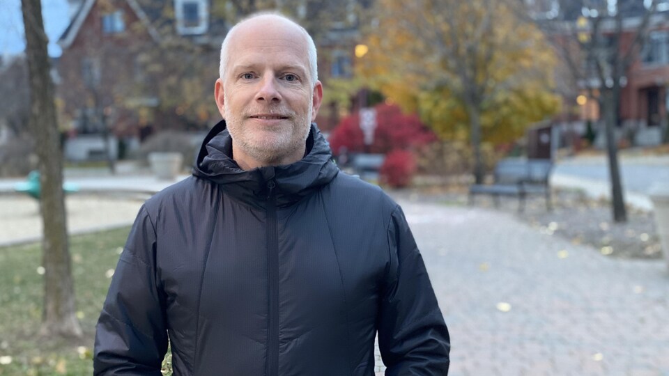 Un homme regardant la caméra devant un parc.