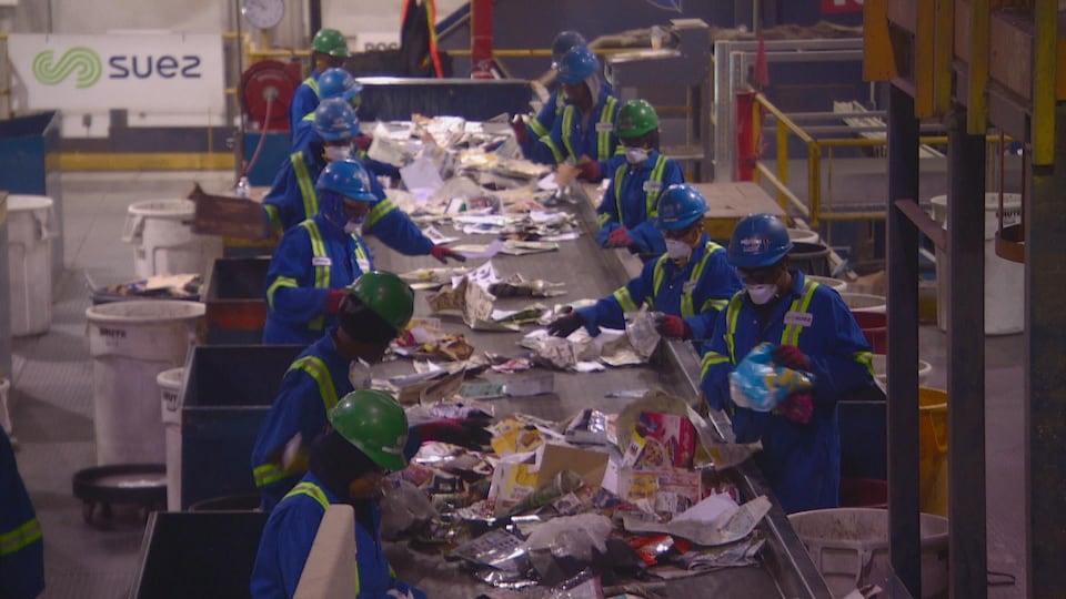Des employés, vêtus d'un habit de protection, qui séparent les matériaux sur une bande roulante.