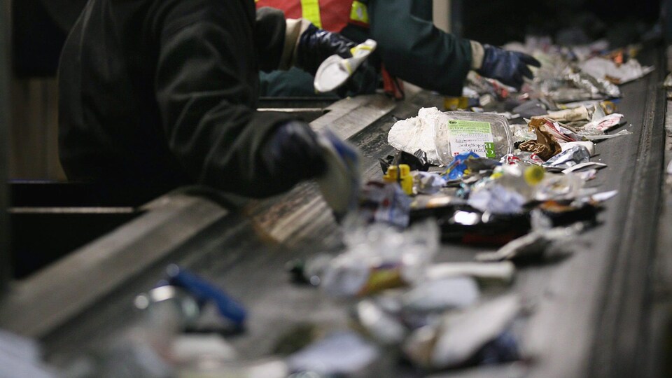 Des employés trient le contenu de bacs de recyclage à une usine.
