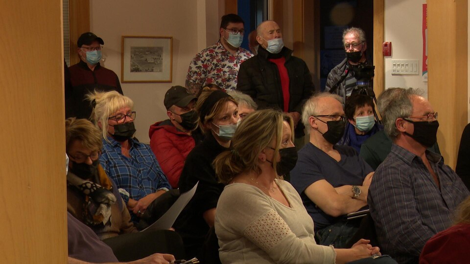 Dans la salle du conseil municipal de Percé, plusieurs personnes portant un masque sont assises ou debout par manque de place.