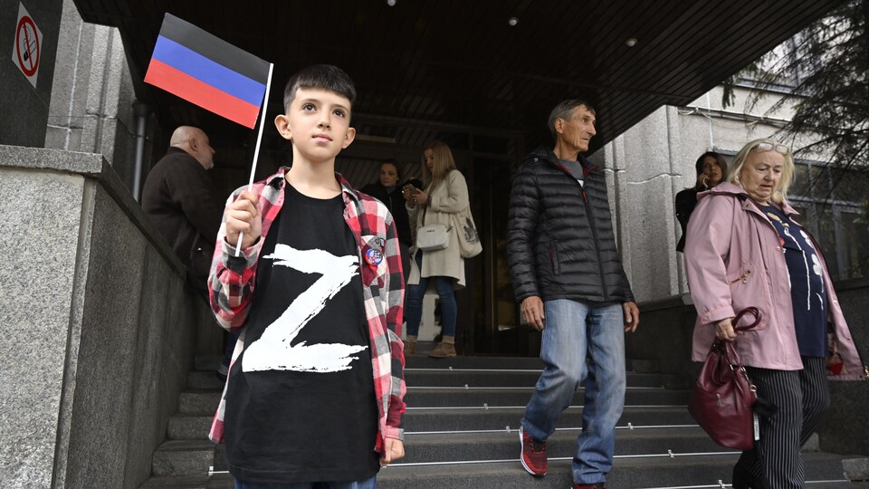 Un garçon portant un t-shirt avec la lettre Z, symbole de soutien à l'armée russe, tient un drapeau de la République populaire autoproclamée de Donetsk.