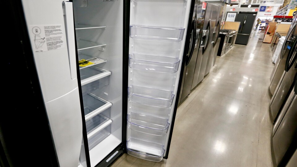Un magasin d'appareils électroménagers, dans la rangée des réfrigérateurs, avec à l'avant-plan un frigo ayant la porte ouverte.