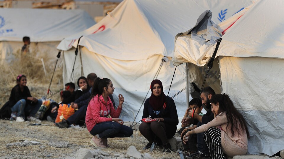 Les membres d'une famille de Syriens sont accroupis près de tentes dans un camp de réfugiés.
