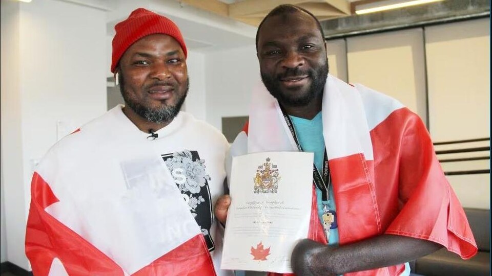 Deux réfugiés drapés dans des drapeaux canadiens montrent un certificat de citoyenneté.
