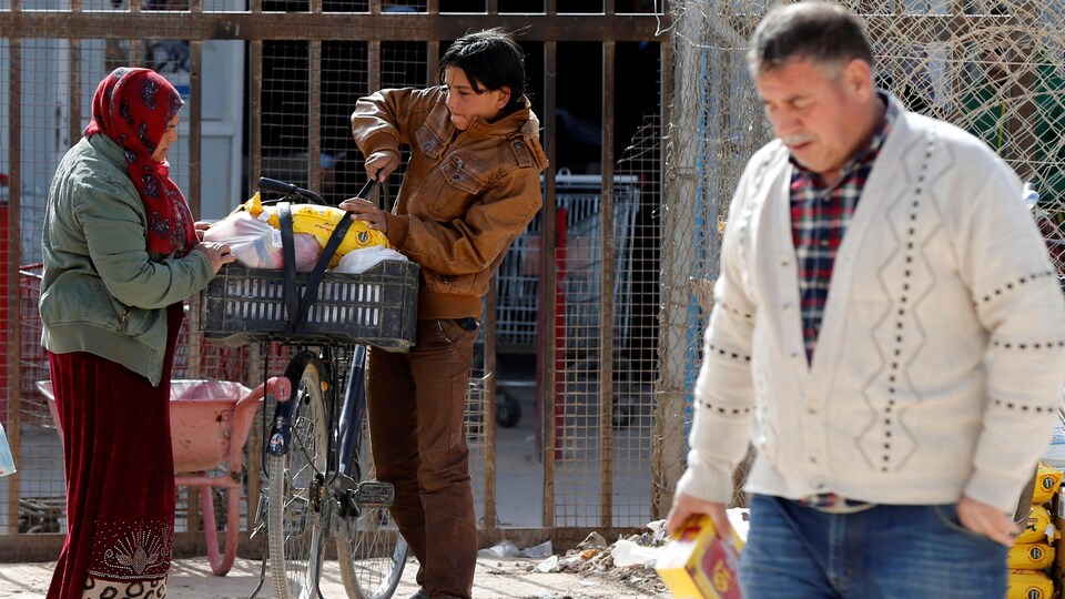 Une femme et son fils lestent de la nourriture dans un panier de bicyclette, alors qu'un homme marche devant eux avec une boîte d'aliments.