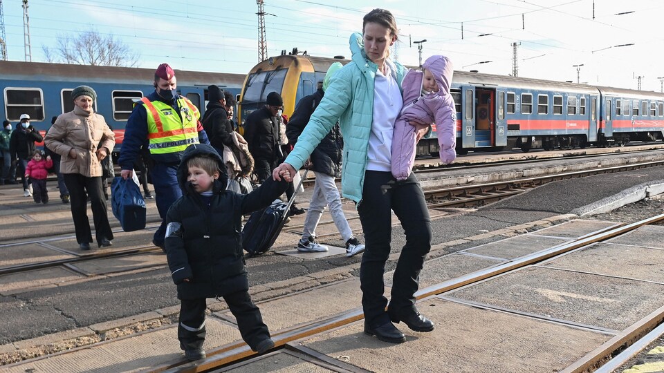 Une femme tenant un bambin dans ses bras, et traînant un enfant avec l'autre, traverse une voie ferrée près du train qui les a amenés en Hongrie.