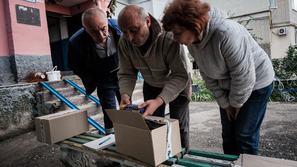 Des civils se regroupent pour partager une boîte d'aide alimentaire et recharger leurs appareils électroniques.