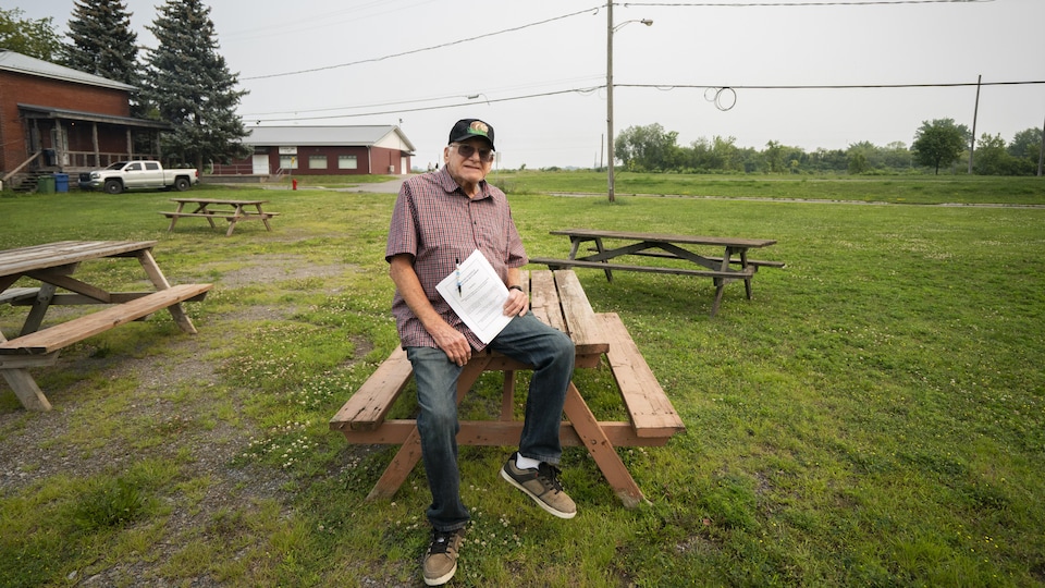 Un homme pose assis sur une table, un document en main.