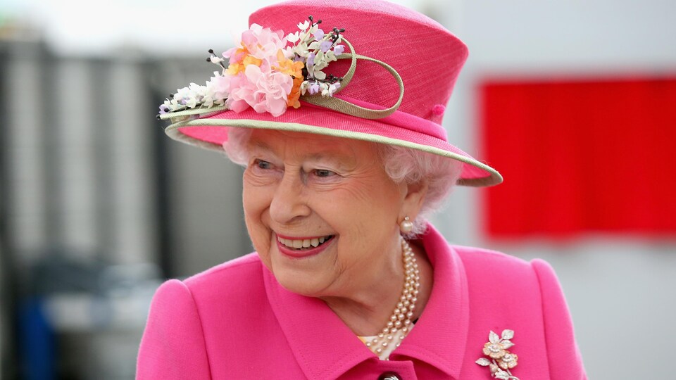 Gros plan sur la reine, souriante et tout de rose vêtue.